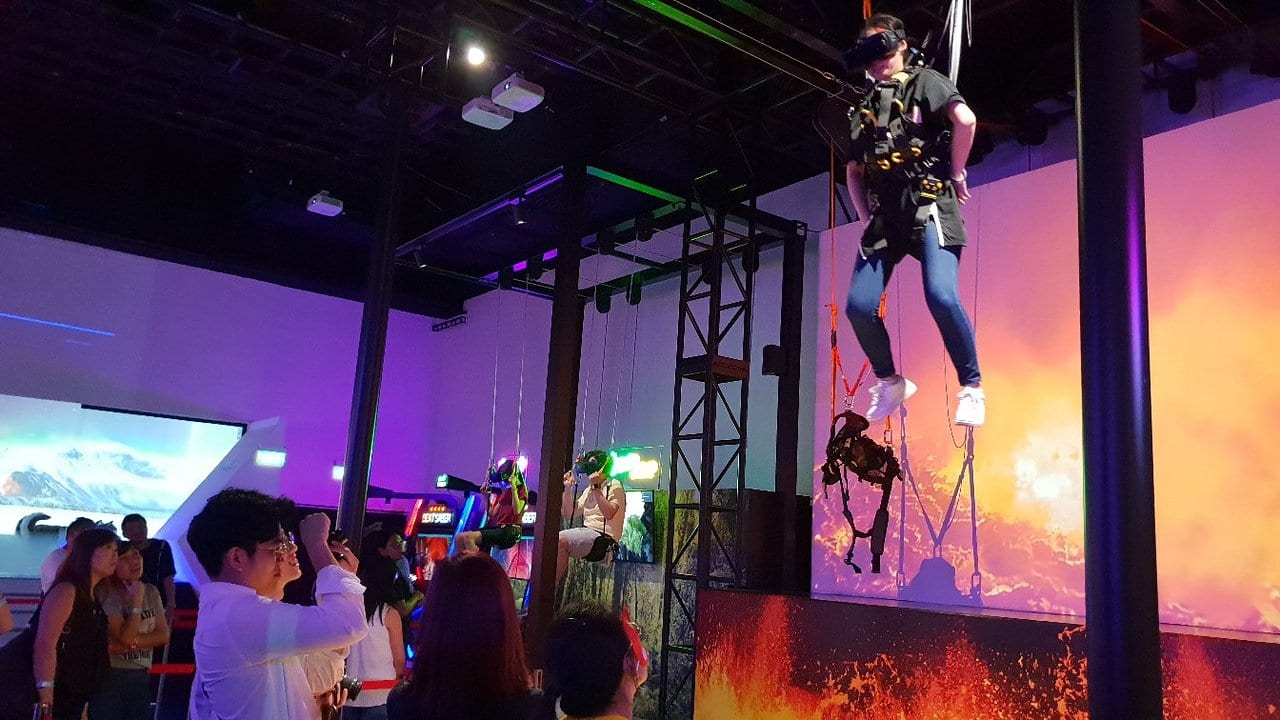 A group of people seeing a young man playing VR games with some accessories to make him fly